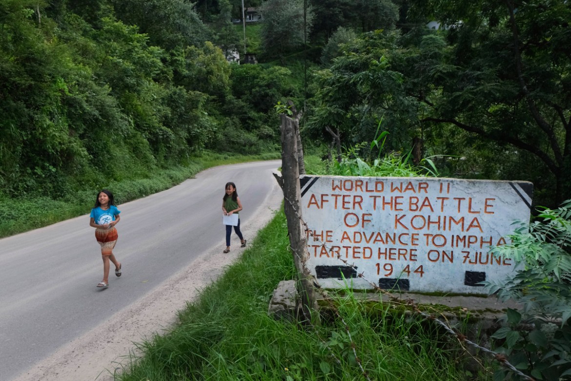 Angami Naga girls walk past a World War II plaque on the Imphal-Kohima highway on the outskirts of Kohima, India, Friday, Aug. 14, 2020. Between April and June 1944, Japanese and British Commonwealth