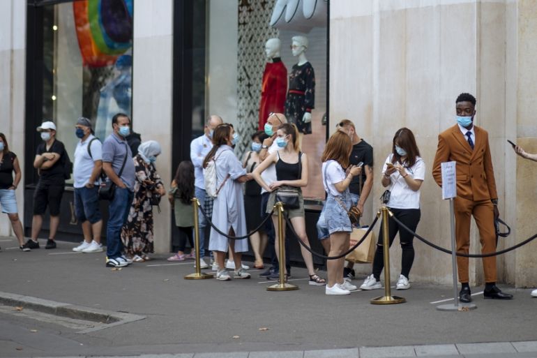 People with face masks queue as they wait to get in the Louis Vuitton shop on the Champs Elysee avenue in Paris, Saturday, Aug. 15, 2020. Paris extended the areas of the city where pedestrians will be