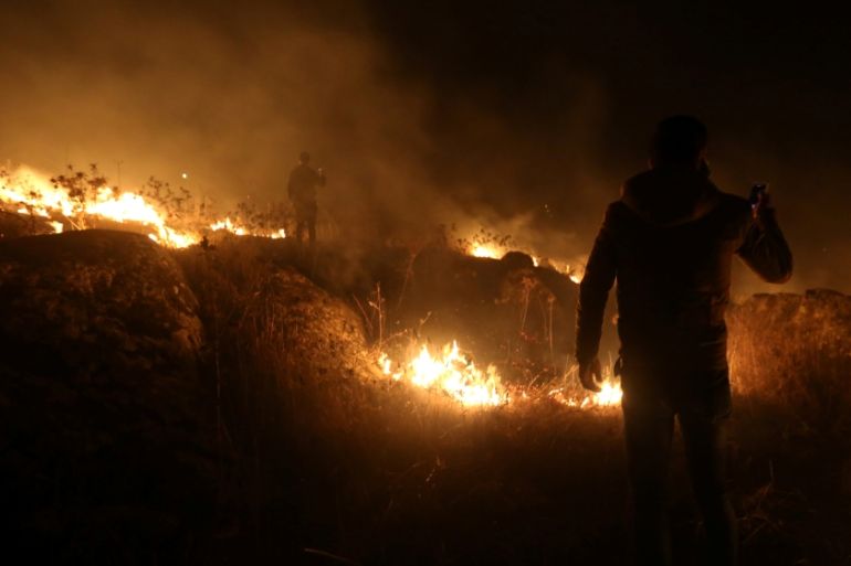 A man uses his phone near a fire in Houla village near the Lebanese-Israeli border, in southern Lebanon