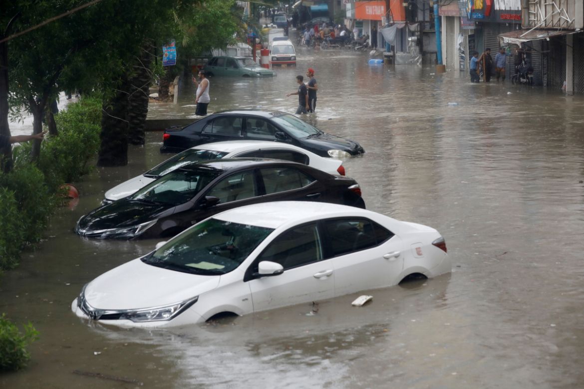 People wade through a flooded street with submerged vehicles during the monsoon rain, as the outbreak of the coronavirus disease (COVID-19) continues, in Karachi, Pakistan August 25, 2020. REUTERS/Akh