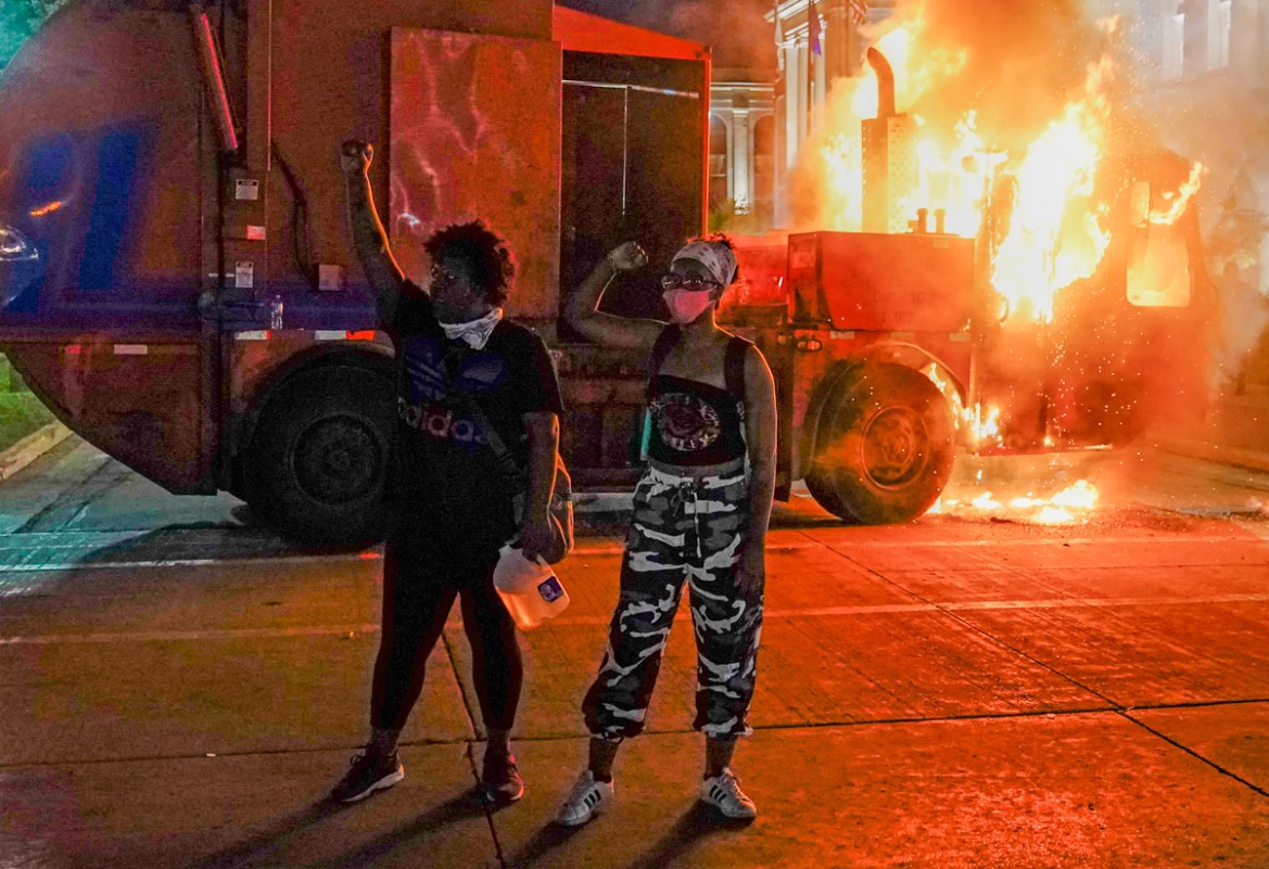 epa08623702 Two protestors stand with raised fists as a garbage truck burns behind them during a second night of unrest in the wake of the shooting of Jacob Blake by police officers, in Kenosha, Wisco