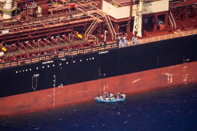Migrants sit in a boat alongside the Maersk Etienne tanker