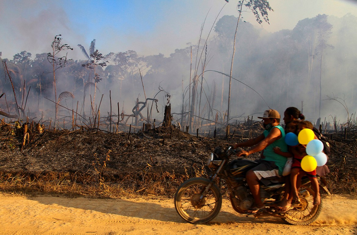 A family rides along a paved dirt road in an area scorched by fires near Labrea, Amazonas state, Brazil, Friday, Aug. 7, 2020. According to the National Institute for Space Research, fires in the Braz