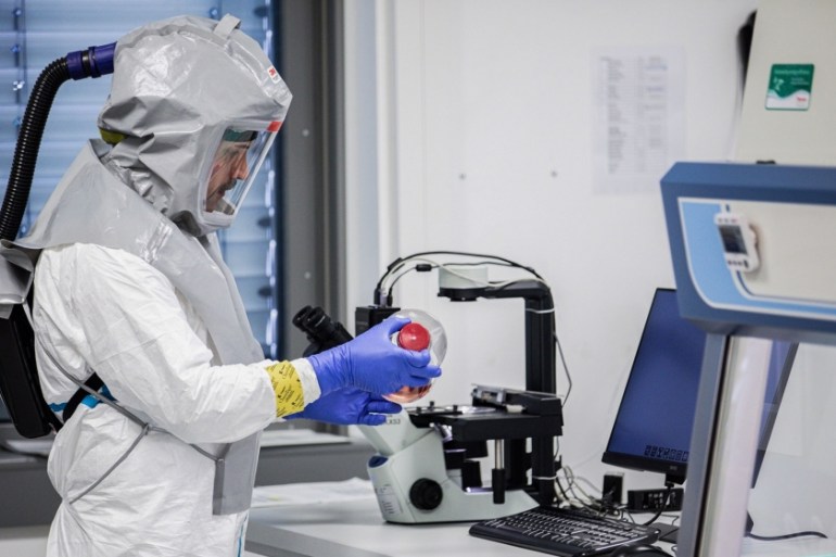 A lab technician wearing a full body protection suit handles a bottle containing growth media for virus production during coronavirus vaccine research at the Valneva SA laboratories in Vienna, Austria