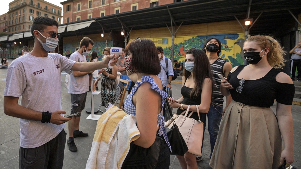 A worker wearing a face mask (L) checks the body temperatures of moviegoers to screen for possible infections with the SARS-CoV-2 coronavirus that causes the pandemic COVID-19 disease on the opening n