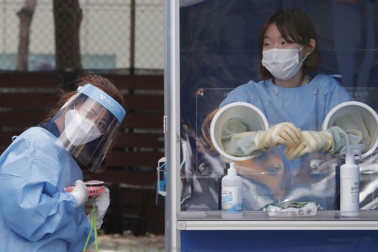 A medical worker holds a portable fan during the sweltering heat while police officers are tested for COVID-19 at a makeshift clinic at the Seoul Metropolitan Police Agency in Seoul, South Korea, Wedn