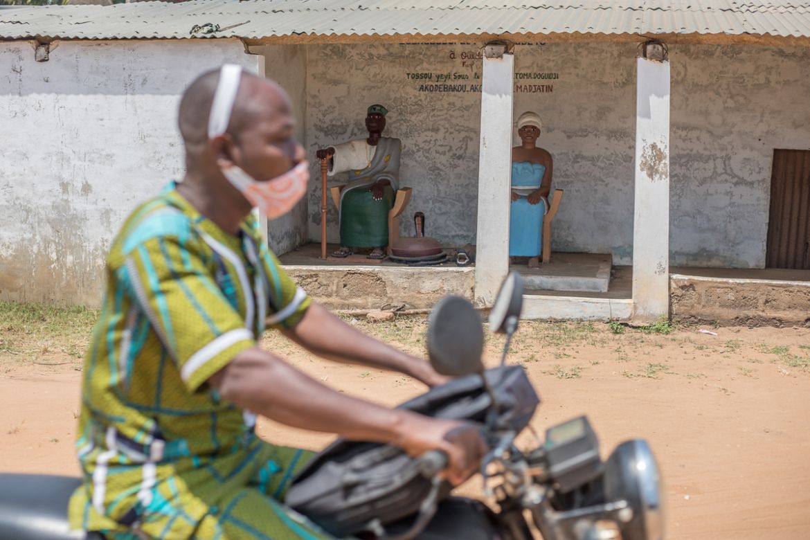 A man drives a motorcycle past a voodoo temple on in Ouidah on August 4, 2020. - As western cities see statues of slaveholders and colonialists toppled, Benin''s coastal town of Ouidah is restoring its