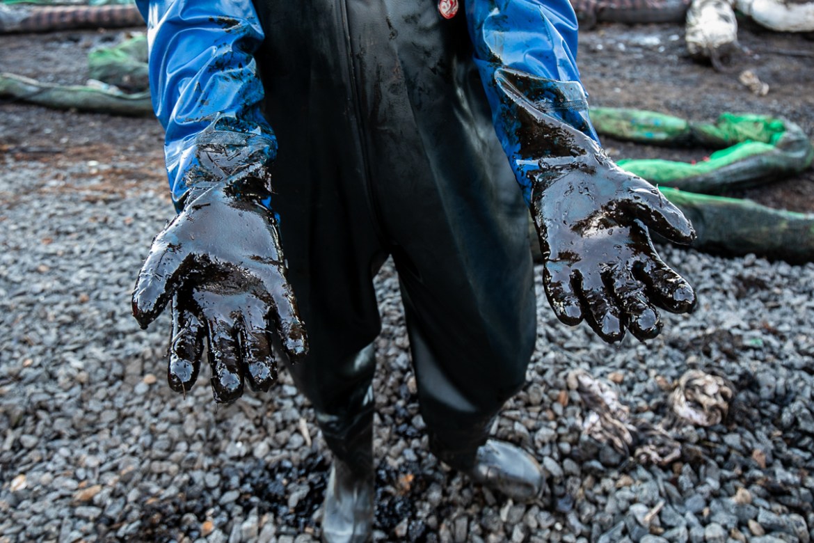 epa08604945 A worker holds out his arms covered in thick oil from collecting seaweed and straw mixed with leaked oil from the MV Wakashio, a Japanese owned Panama-flagged bulk carrier after it ran agr