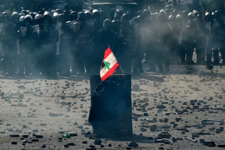 epa08592182 An anti-government protester carries a Lebanese flag as he protects himself behind an iron barrel during a protest outside of the Lebanese Parliament in Beirut, Lebanon, 08 August 2020. Pe