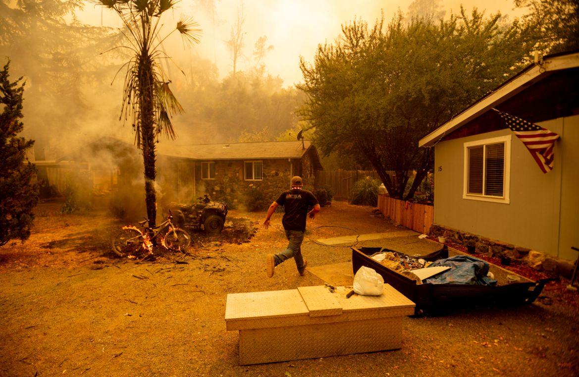 A resident runs into a home to save a dog while flames are getting close as the Hennessey fire continues to rage out of control near Lake Berryessa in Napa, California on August 18, 2020. - As of the