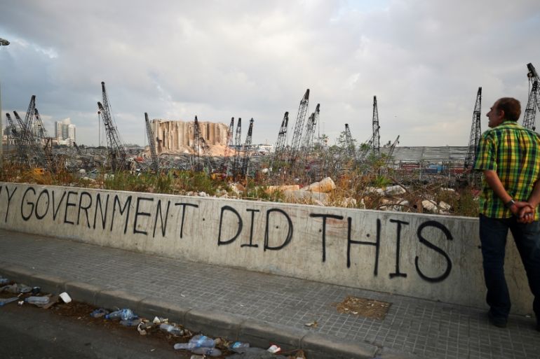 A man stands next to graffiti at the damaged port area in the aftermath of a massive explosion in Beirut