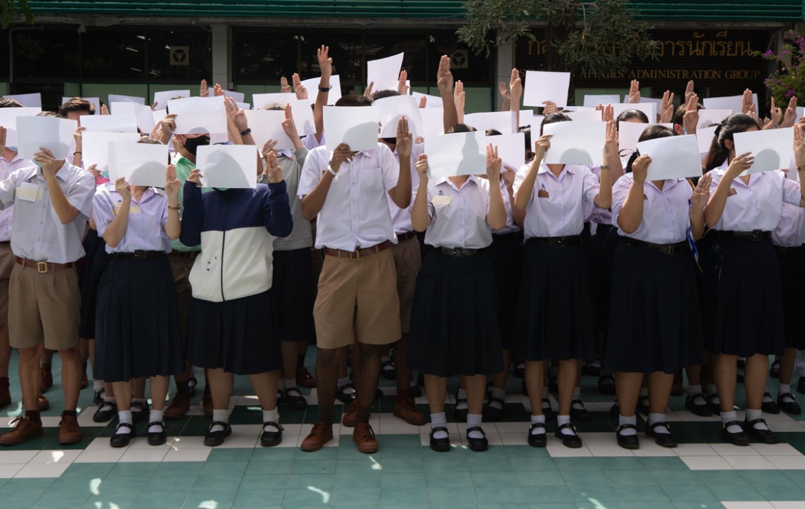 High school students hold up blank sheets of paper and raise their hands with a three-fingered defiance salute at the Samsen Wittayalai school in Bangkok, Thailand on Tuesday, Aug. 18, 2020. A number