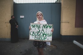 Valeria, 19, a student poses for a photo holding a handmade poster that reads "Peaceful people for the free choice" during an opposition rally in front of a detention center in Minsk, Belarus, Monday,