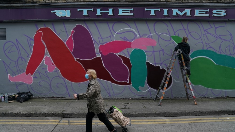 A woman wearing a protective face mask walks past a man painting a mural, amid the coronavirus disease (COVID-19) outbreak, in Dublin, Ireland, August 20, 2020. REUTERS/Clodagh Kilcoyne
