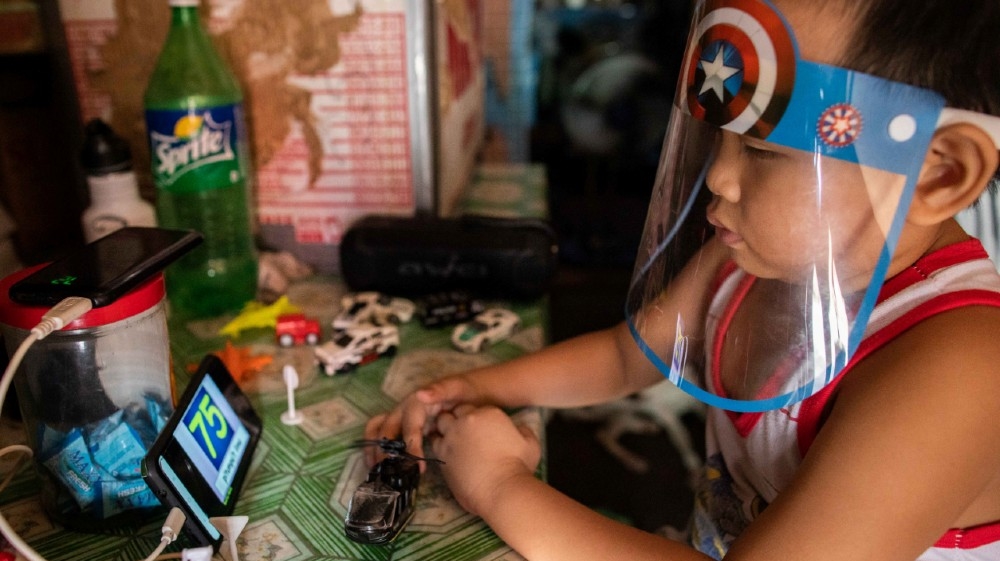 A boy wears a face shield while watching a simulation of an online learning class from a smartphone in his home, amid the coronavirus disease (COVID-19) outbreak in Manila, Philippines,