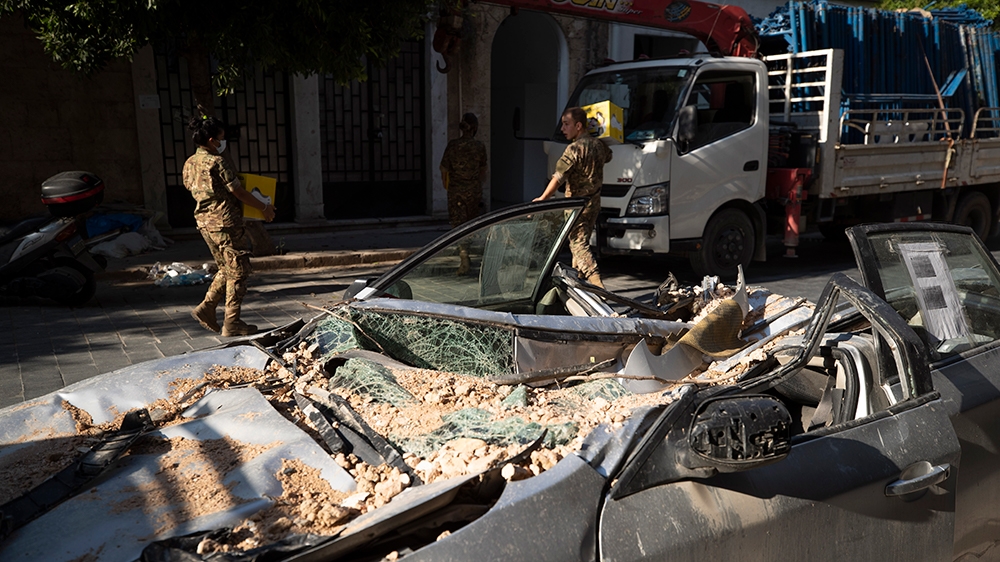 Lebanese army soldiers hold aid boxes past a destroyed car near the scene of last week's explosion that hit the seaport of Beirut, Lebanon, Wednesday, Aug. 12, 2020. (AP Photo/Hassan Ammar)