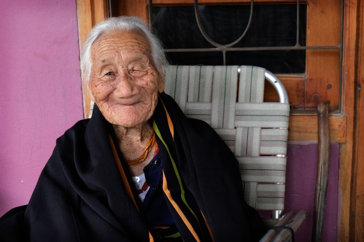 Kuou Kesiezie, a 108-year-old Angami Naga survivor of the Battle of Kohima fought between the Japanese and British Commonwealth forces in and around her village, smiles as she sits outside her daughte