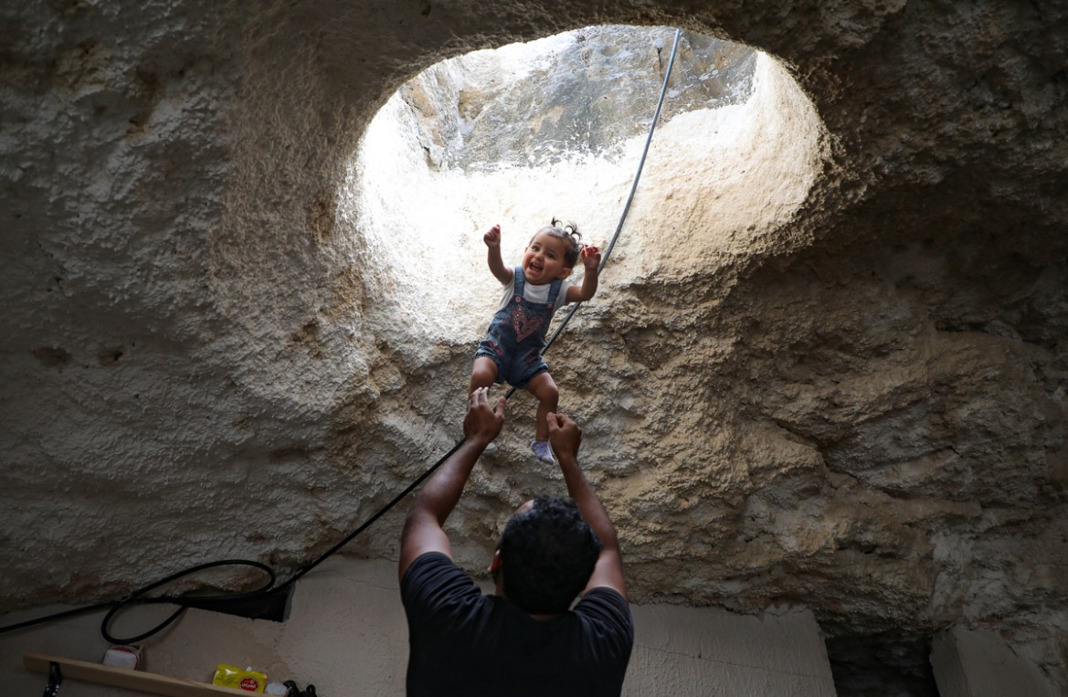 Ahmed Amarneh throws his daughter beneath a skylight hole as they play together at his home, built in cave in the village of Farasin, west of Jenin, in the northern occupied West Bank on August 4, 202