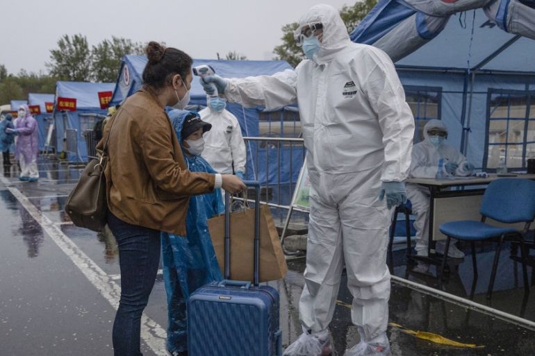 A worker in protective overalls take the temperature of a traveler from Wuhan before directing her to her district in Beijing on Sunday, April 19, 2020. Wuhan, the city at the center of the global cor