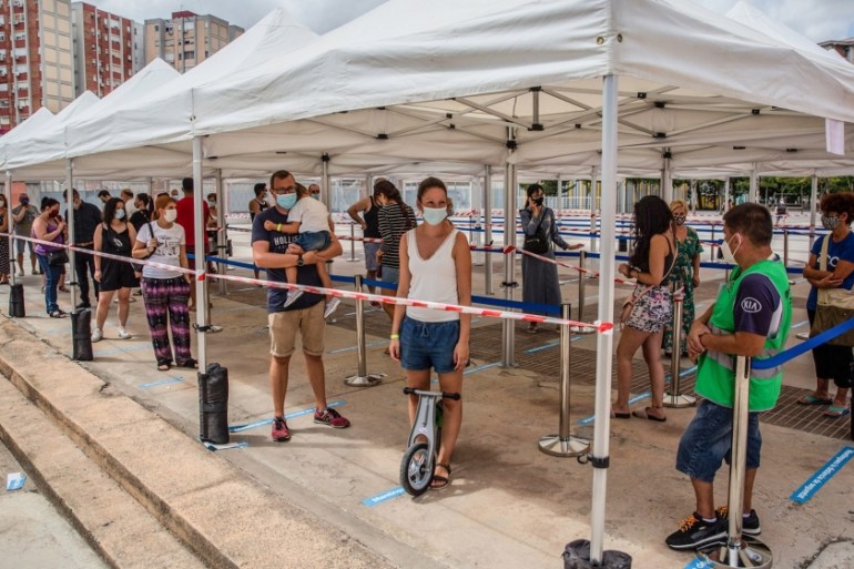 Residents wearing protective face masks queue at social distancing markers outside a mass coronavirus screening facility in the Sant Ildefons district of Barcelona, Spain, on Tuesday, Aug. 25, 2020. S