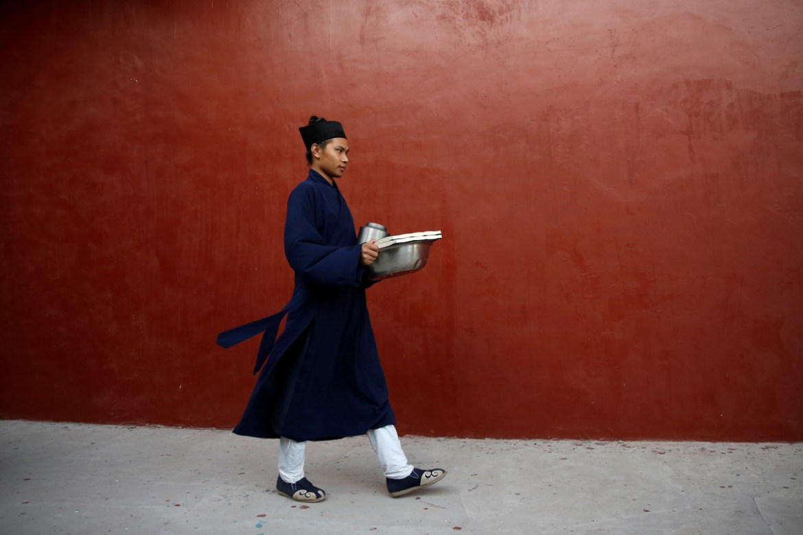 Priest Xia Shiran, 25, holds scripture books and offerings in preparation for a memorial ceremony on the day of Hungry Ghost Festival, at Taoist temple Jiuyang Palace, in Laiwu of Jinan city, Shandong
