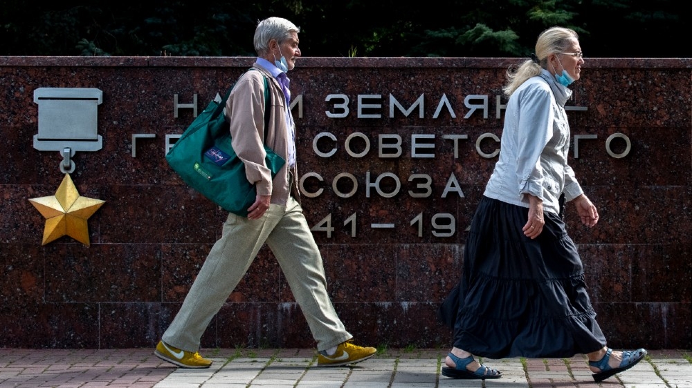 A woman and a man wearing face masks to protect against the coronavirus disease walk past a WWII monument in the town of Chekhov, some 70 km outside Moscow, on August 27, 2020. Yuri KADOBNOV / AFP