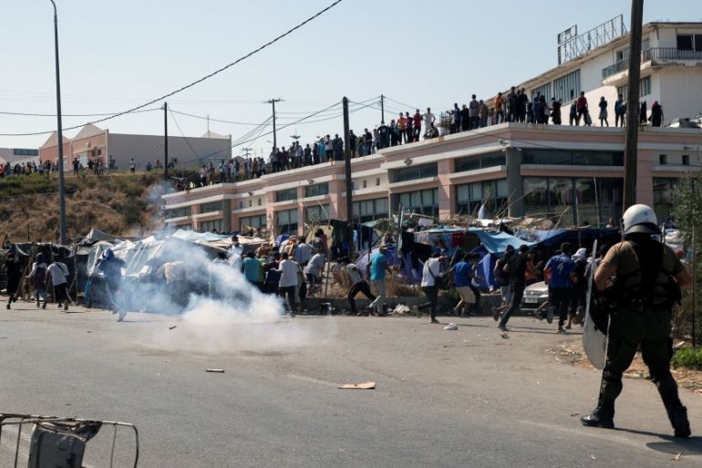 Refugees and migrants flee tear gas fired by riot police during clashes, on the island of Lesbos