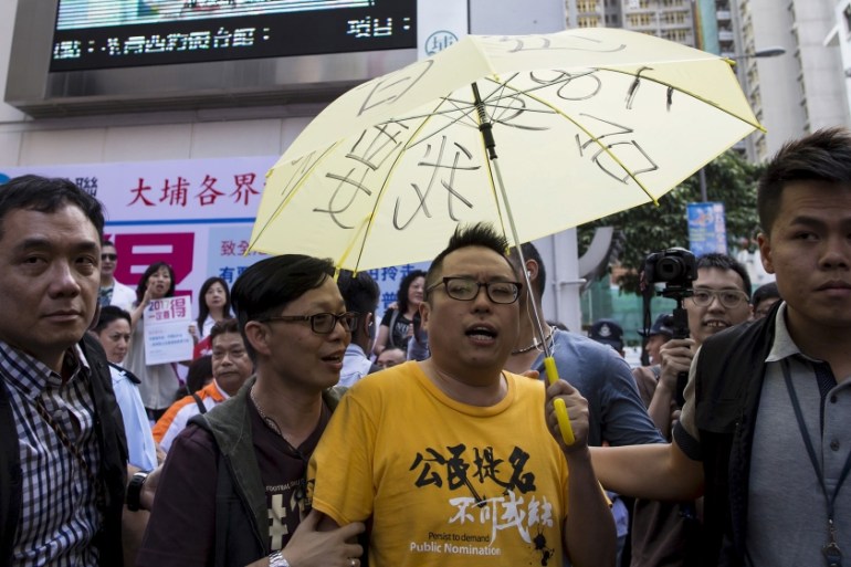 Pro-democracy activist Tam Tak-chi holds a yellow umbrella, the symbol of the Occupy Central movement, as he is escorted away by police after confronting government supporters as Chief Secretary Carri