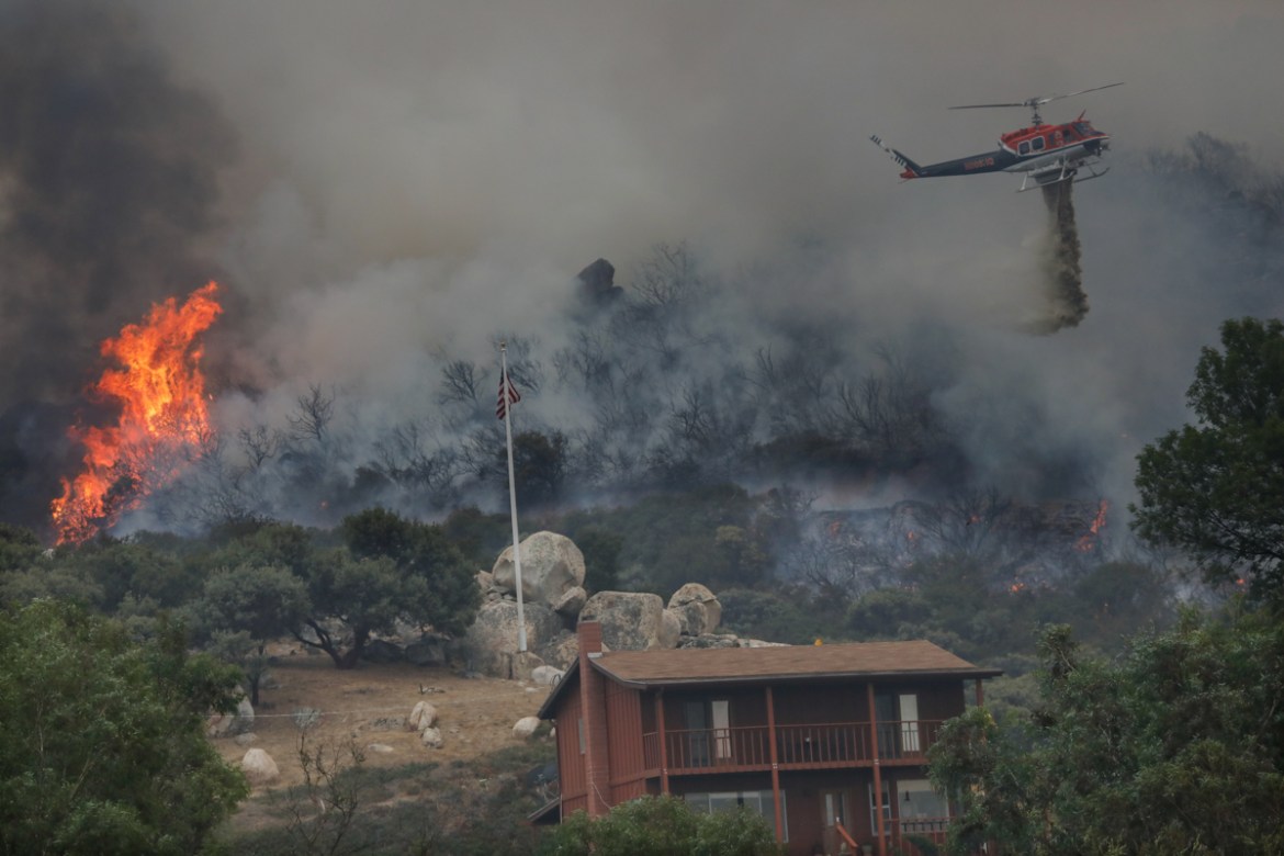 A brush fire encroaches along Japatul Road as a helicopter drops water during the Valley Fire in Jamul, California on September 6, 2020 - The Valley Fire in the Japatul Valley burned 4,000 acres overn