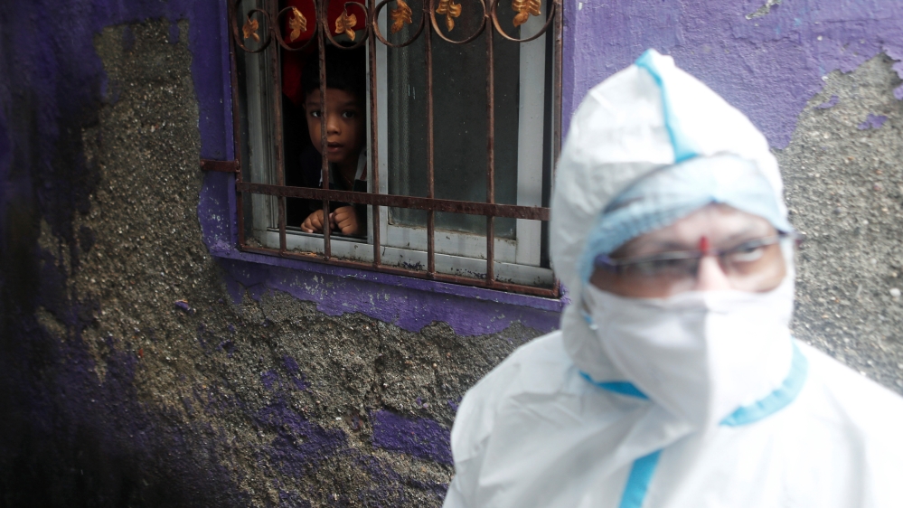 A boy watches a health worker in personal protective equipment (PPE) as she walks past a house during a check up campaign for the coronavirus disease (COVID-19), in Mumbai