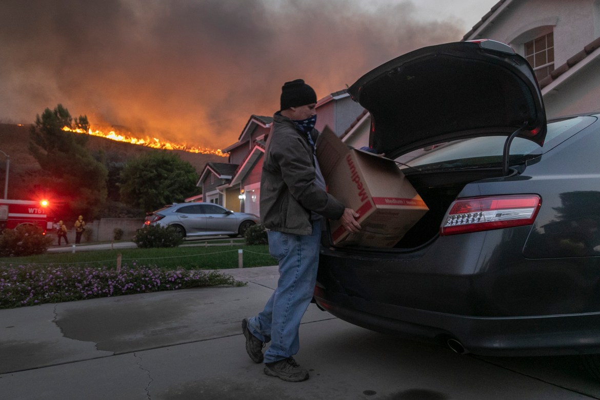 Um homem evacua quando as chamas chegam perto de casas em Chino Hills, Califórnia.  [David McNew / Getty Images / AFP]