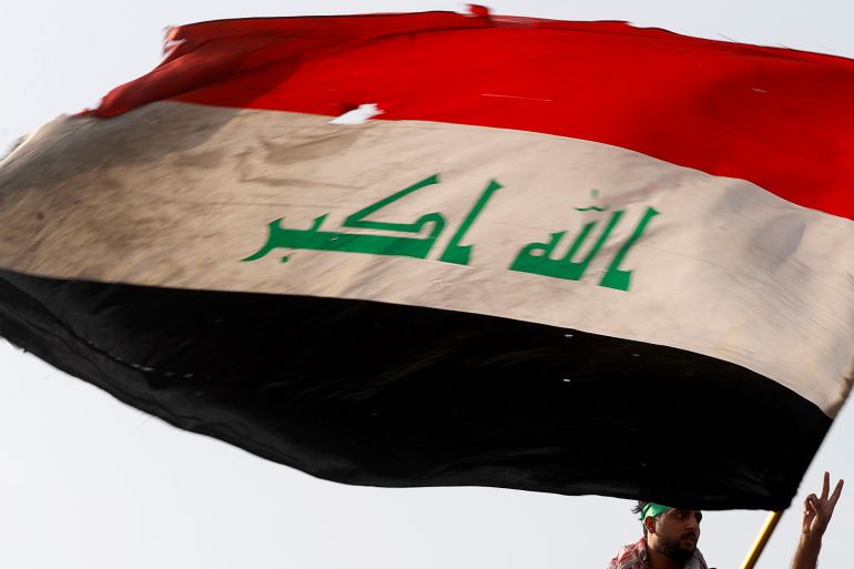 A demonstrator holds an Iraqi flag as another gestures while they gather to mark the first anniversary of the anti-government protests in Baghdad