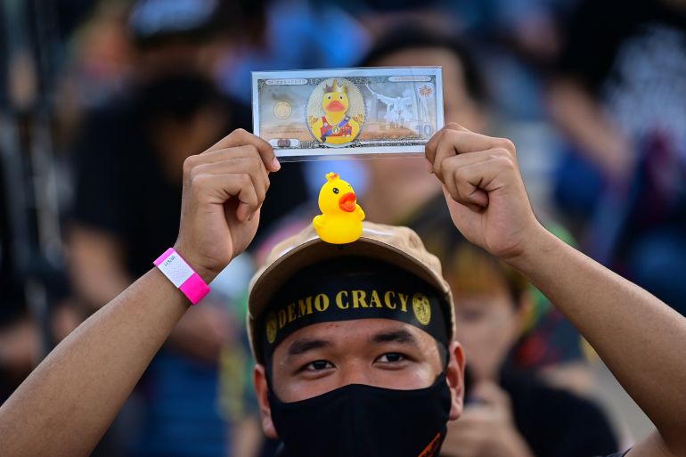 A pro-democracy protester with a small rubber duck displayed on his cap holds up a mock banknote during an anti-government rally outside the headquarters of the Siam Commercial Bank in Bangkok on November 25, 2020. (Photo by Lillian SUWANRUMPHA / AFP)
