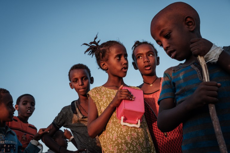 Ehiopian children who fled Tigray wait for food to be distributed in front of a warehouse at Um Raquba refugee camp in Gadaref, eastern Sudan [Yasuyoshi Chiba/AFP]
