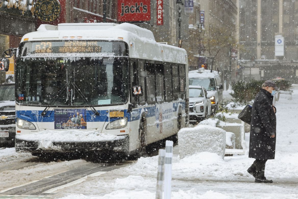 A pedestrian walks past a bus while snow falls in New York as temperatures dropped to 27 degrees fahrenheit (2 degrees Celsius) with frigid sustained winds up to 56 km/h (35 mph). [Angus Mordant/Bloomberg]