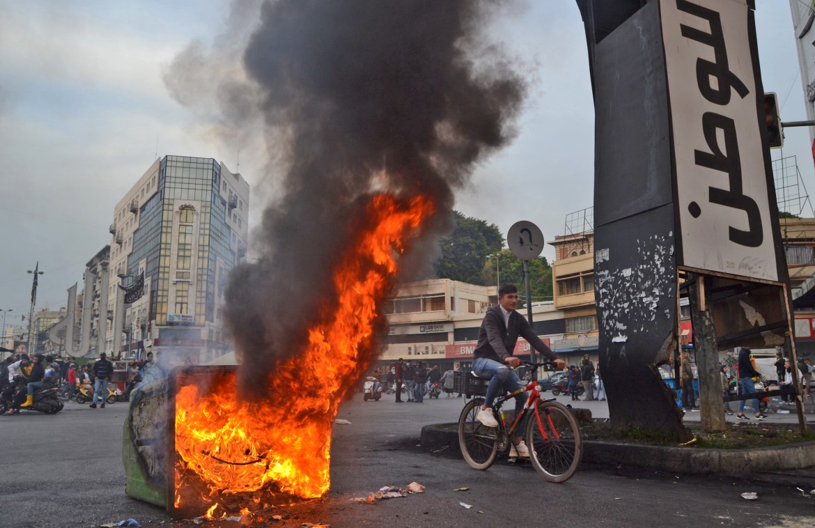 A Lebanese youth rides his bicycle by a dumpster set on fire by protesters gathered at Al-Nour Square. [Fathi al-Masri/AFP]