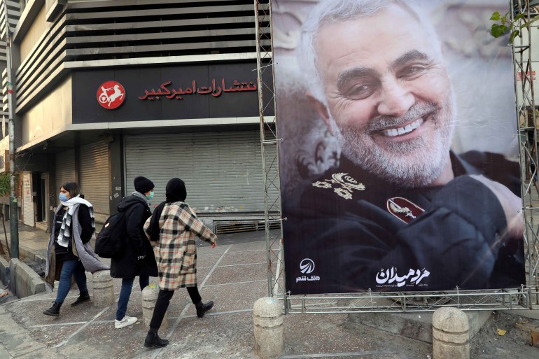 People in Tehran walk near a poster of General Qassem Soleimani,