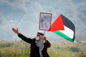 A demonstrator holds a banner and Palestinian flag during a protest against the building of illegal Israeli settlements in Beit Dajan in the Israeli-occupied West Bank on January 8, 2021 [Raneen Sawafta/Reuters]