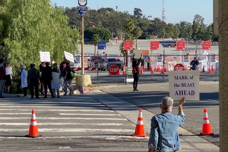 Protesters hold placards near the entrance of vaccination centre at Dodger Stadium [Twitter @DAVEEDKAPOOR via Reuters]