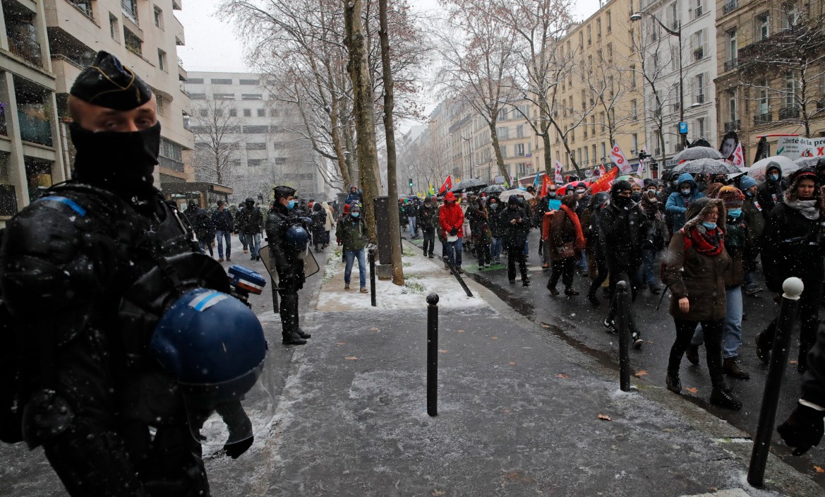 Police officers watch as protesters march in Paris. The protesters are also against the use of ramped-up surveillance tools. [Christophe Ena/AP Photo]