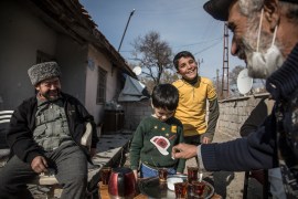Taufeeq, 55, a Syrian refugee, serves hot black tea to his Uighur neighbour outside his home in Kayseri, Turkey, as his son Moaaz and other children return after playing football [Ahmer Khan/Al Jazeera]