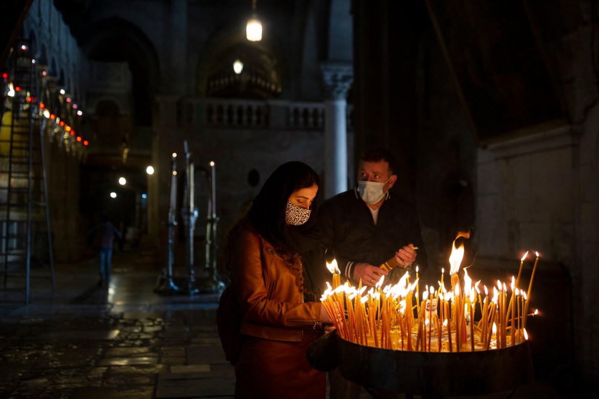 A couple lights candles during Palm Sunday mass in the Church of the Holy Sepulchre in the Old City of Jerusalem. [Maya Alleruzzo/AP Photo]