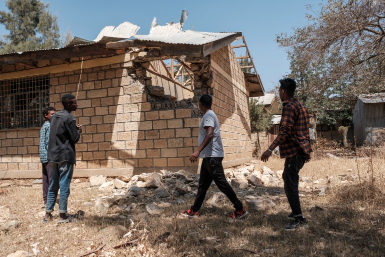 People stand next to a damaged building at Ksanet Junior Secondary School, which was shelled as federal-aligned forces entered the city and allegedly looted by Eritrean forces in Wukro, north of Mekelle [File: Eduardo Soteras/AFP]
