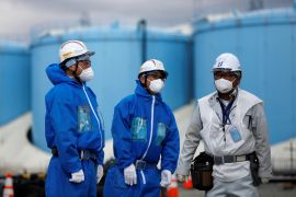 Workers in blue overalls, hard hats and masks in Fukushima. Behind them are the tanks contained the treated radioactive water