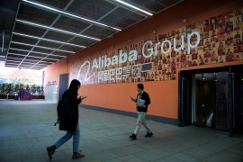 Two people walking by a wall decorated with the Alibaba Group's logo.