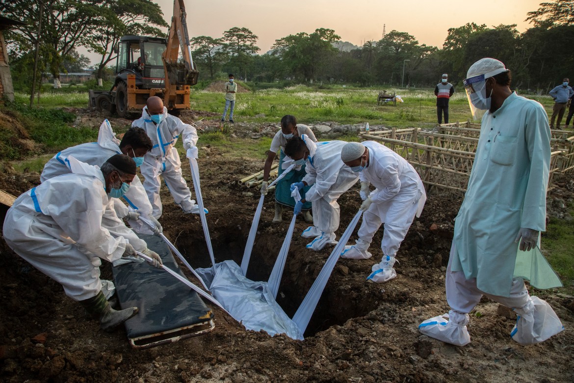 Relatives and municipal workers in protective suits bury the body of a person who died due to COVID-19 in Guwahati city. [Anupam Nath/AP Photo]