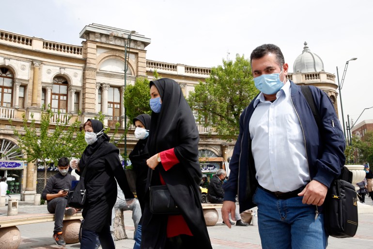 Iranians wearing face masks walk on the street
