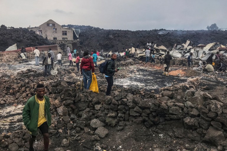 Residents are seen standing next to destroyed structures near smouldering ashes early morning in Goma in the East of the Democratic Republic of Congo [Moses Sawasawa / AFP]
