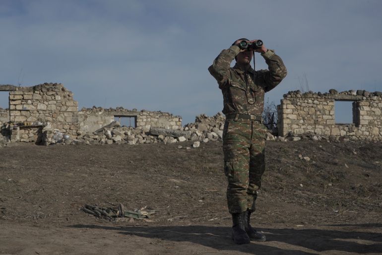 An ethnic Armenian soldier looks through binoculars as he stands at fighting positions near the village of Taghavard in the region of Nagorno-Karabakh, January 11, 2021.