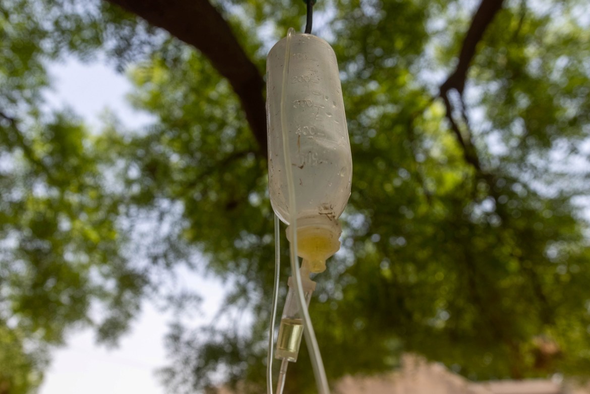 An infusion bag attached to a tree branch is seen at the makeshift open-air clinic. [Danish Siddiqui/Reuters]